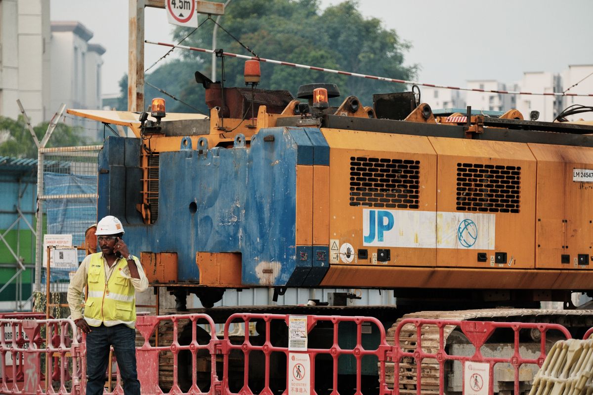 Construction worker on a phone in front of plant machinery at an active building site